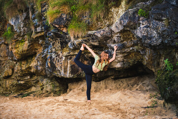 Teenage girl with long red hair practicing ballet poses by colorful rock formation on sandy beach
