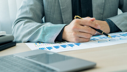 Businessman holding pen pointing to graph while analyzing financial paper graph and on desk at office