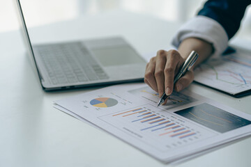 Businessman holding pen pointing to graph while analyzing financial paper graph and on desk at office