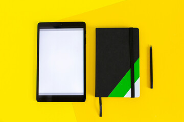 Home office flat lay with tablet and black notebook on yellow background