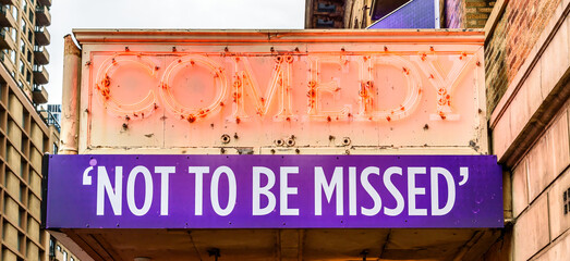 A COMEDY, NOT TO BE MISSED sign with red neon letters and white on purple letters