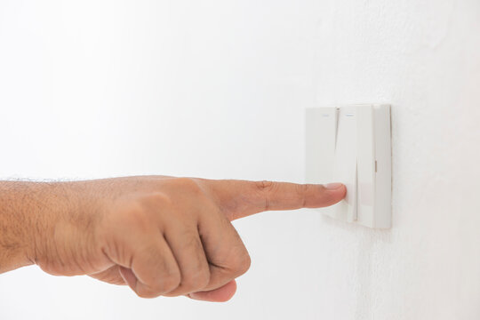 Close-up light switch of a male finger will turn on or off a light switch with white wall at home. white plastic mechanical switch mounted. Energy, energy, save electricity, copy space