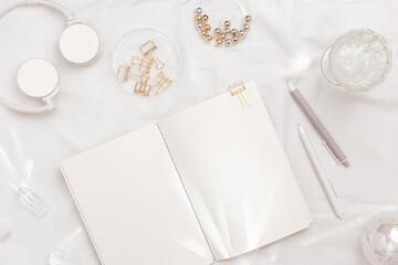 New Year planning, open blank page copybook, pen, gold metallic color paper clips, glare crystal stone with light beams, christmas decor on white bed. Aesthetic flat lay, concept female work