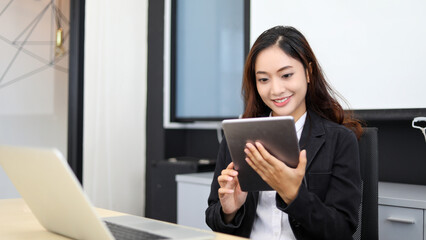 Smiling Asian businesswoman using tablet for work and Cute girl searching for some data and concentrate on her tablet in her office.