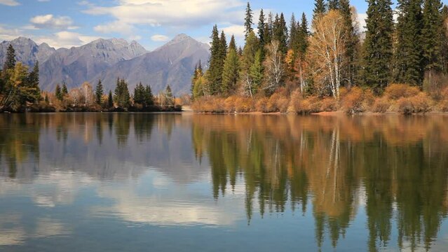 Close-up  view of clear water and small ripples of Irkut River with yellowed trees on shore and the mountains of Eastern Sayan in distance on sunny September day. Beautiful autumn calm landscape