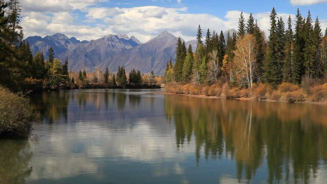 Picturesque autumn landscape with reflection of clouds, mountains and yellowed forest in calm blue water of Irkut River. Baikal region, Buryatia, Tunka foothill valley