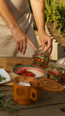 a woman preserves sun-dried tomatoes in sterile jars with chopped garlic and fresh basil in the garden at sunset. hands close-up, rich harvest, organic natural products, preparations for the winter