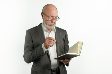 An elderly man in a suit with a notebook and a pen is thinking about a task. on a white background