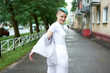 A woman with green hair in white clothes and with an umbrella walks down the street after the rain