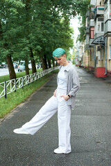 A woman with green hair in white clothes and with an umbrella walks down the street after the rain
