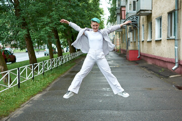A woman with green hair in white clothes and with an umbrella walks down the street after the rain