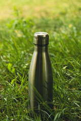 Water bottle. Reusable steel thermo water bottle on green grass. Sustainable lifestyle. Plastic...