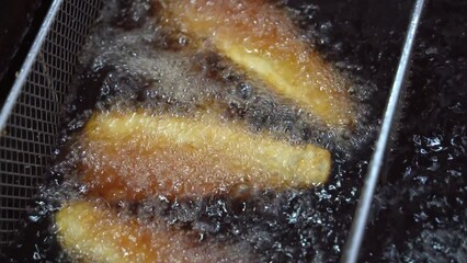 Golden delicious crispy fish fillet, traditional fish and chips cooking in progress, deep frying in boiling hot oil fast food commercial kitchen, night market pub food, close up shot.