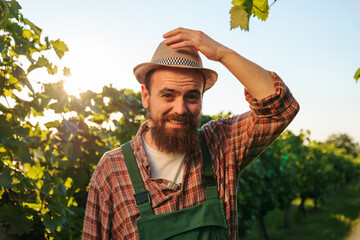 Front view looking at camera young farmer male vineyard worker winemaking smiles broadly and holds...