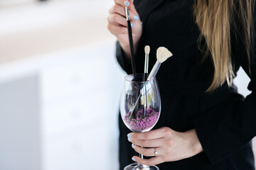 Makeup tools. Makeup concept. The girl is holding a glass in which there are brushes. Brushes for the face.
