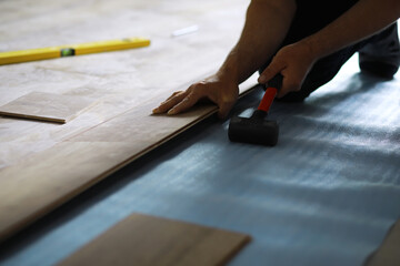 Installing laminated floor, detail on man hands blue wooden tile, over white foam base layer, small pile with more tiles background