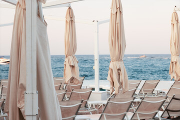 Fototapeta na wymiar Closed beach umbrellas and deck chairs on a summer evening the end of the season