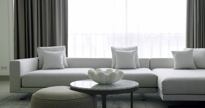 Minimalist living room with white furniture and round table. Luxury Modern House Interior With Corner Sofa and Bookshelf. Fashionable furniture. Minimalist Home Interior. Cozy Modern Furniture Design.