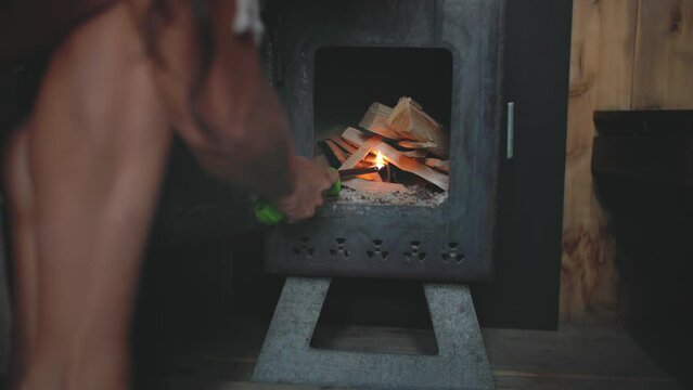 Woman lights fire in sauna wood stove