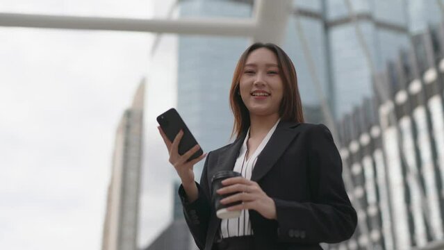 4K video of a professional smart cool asian young attractive businesswoman holding a cup of coffee look around the city with happy satisfied look after finish chatting happily on the phone in a centra