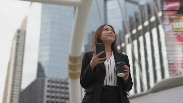 4K video of a professional smart cool asian young attractive businesswoman holding a cup of coffee look around the city with happy satisfied look after finish chatting happily on the phone in a centra