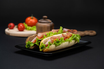 Still life with tasty sandwiches with ham, cheddar and vegetables in black plate on a black background