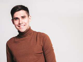 Portrait of handsome smiling model. Sexy stylish man dressed in brown turtleneck sweater and jeans. Fashion hipster male