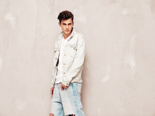 Portrait of handsome confident stylish hipster lambersexual model.Man dressed in jacket and jeans. Fashion male posing in studio near grey wall