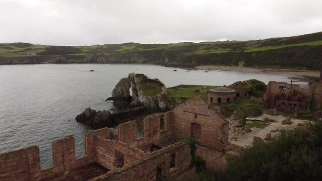 Reverse aerial view descending across Traeth Porth Wen Beach bay abandoned brickwork factory on the Irish sea coast