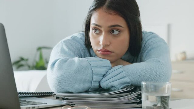 Documents, report and bored with a woman entrepreneur remote working on a laptop in her home office. Paperwork, startup and waiting with a female employee at work at a desk in her small business