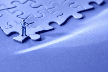 Single tiny worker miniature figure on edge of linked jigsaw puzzle. Monochrome blue background....