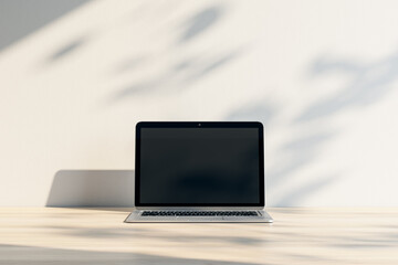 Close up of laptop with empty screen and mock up place at wooden workplace with shadows. 3D Rendering.