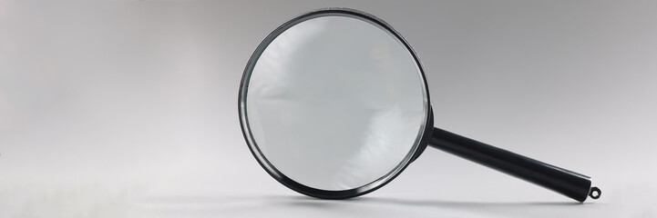 Single magnifying glass with black handle, leaning on grey surface
