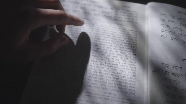 Person's Finger Points On Verses In An Open Hebrew Bible Or Tanakh With Streaks Of Sunlight. close up