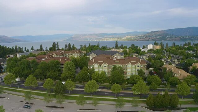 Drone view ascends over townhouses and condos to reveal the Okanagan Lake and distant mountains in Kelowna.