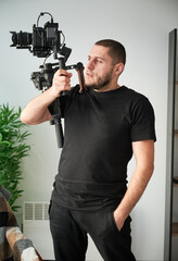 Portrait of videographer man posing indoors with camera mounted on gimbal stabilizer equipment.