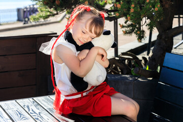 Girl with red pigtails in the park in summer with a panda toy bear