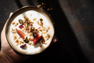 Eine Hand hält eine Frühstück Schüssel mit Müsli, Joghurt und frischen Feigen. Draufsicht.