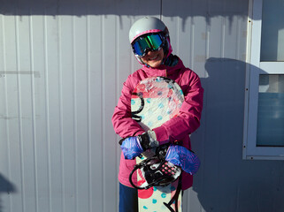 Winter sport woman posing with snowboard on the background of ski pass office. Woman snowboarder...