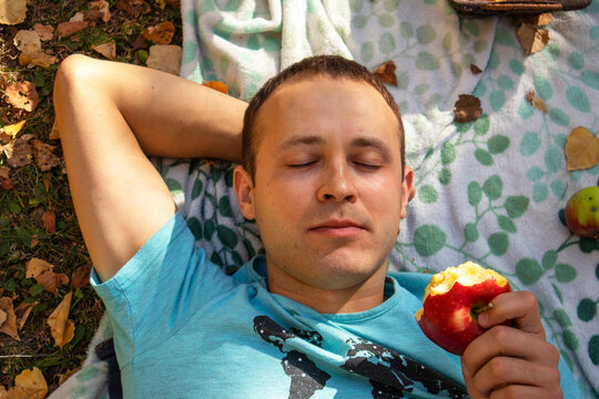 the man is lying on a blanket and eating an apple at a picnic in the fall