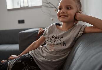 Beautiful little girl sitting on cosiness sofa in the living room at home and watching TV