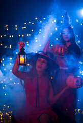 Happy Halloween! Young caucasian woman holding candle lantern and a big pumpkin carved into a face, enjoy halloween party decorated with smoke fog and flashing lights.