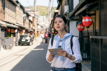 confused asian Japanese woman backpacker looking into distance and wondering which way to go while using map to find destination on Gion Hanamikoji Street in Kyoto japan - obrazy, fototapety, plakaty