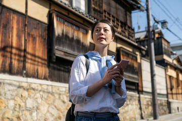 Fototapeta premium asian Japanese girl tourist looking into distance to make sure the way she should go while using navigation app on the phone during her visit to Gion Hanamikoji Street in Kyoto japan.
