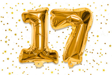 The number of the balloon made of golden foil, the number seventeen on a white background with sequins. Birthday greeting card with inscription 17. Numerical digit, Celebration event.