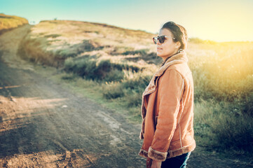 Naklejka premium Lifestyle of a Latin girl on a road outdoors. Portrait of a young woman on a road, Close-up of a young woman on the road, woman on a road. Latina girl woman concept on a dirt road