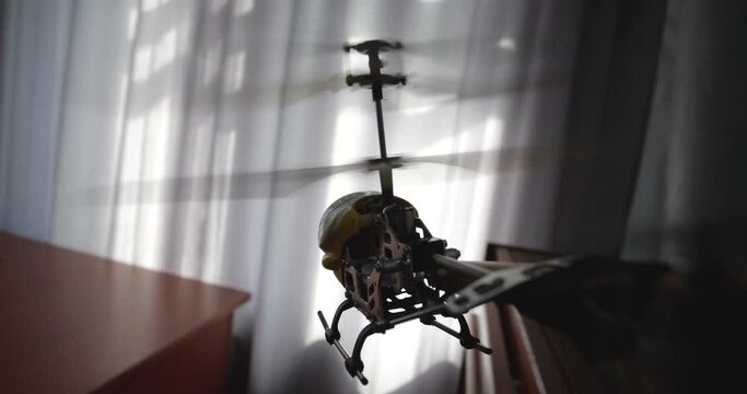 Point of view video of toy yellow radio-controlled model  helicopterflying and landing on children's desk with drawings, pencils and scissors. Window is in the background. Slow motion 50 fps