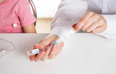 A doctor is putting a drug into a nebulizer for the treatment of respiratory diseases in a little...