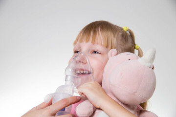 A little girl 5 years old in a pink T-shirt breathes into a nebulizer for lung disease. Treatment...