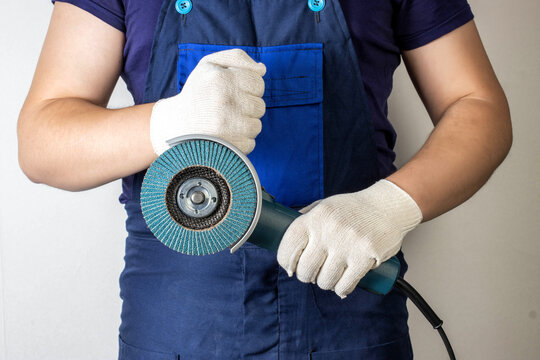 Angle grinder in the hands of a working man against the background of blue overalls. Industry